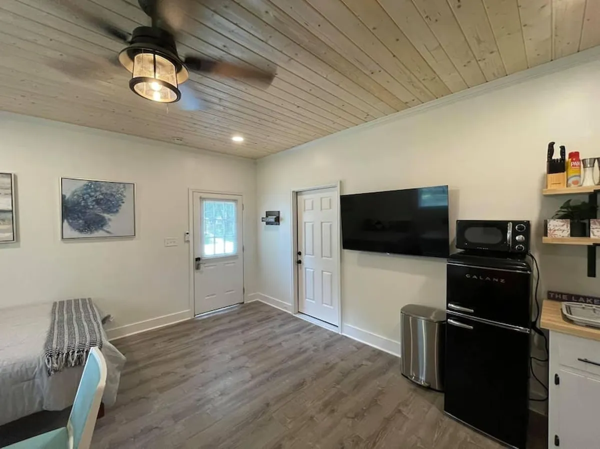 A view of the kitchen area seamlessly flows into a small dining space with a table and chairs, an entrance door, and a TV mounted on the wall. This image captures a cozy, functional environment where cooking, dining, and entertaining can all take place within a compact layout.