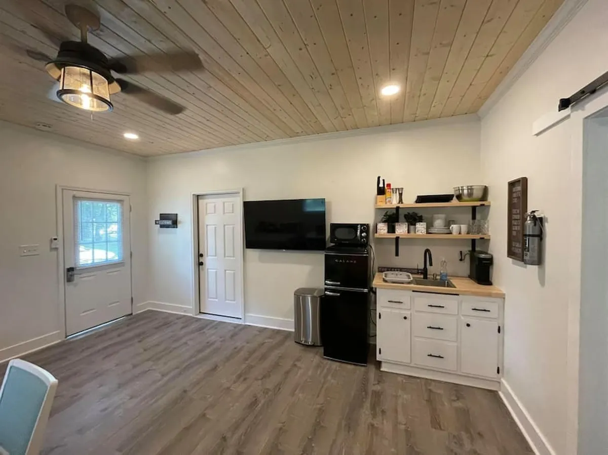 A view into the living space featuring a kitchenette, a television (likely a Roku TV), and doorways that expand the sense of space. The TV is positioned for easy viewing from the living area, and the design remains casual and comfortable, with subtle modern touches.